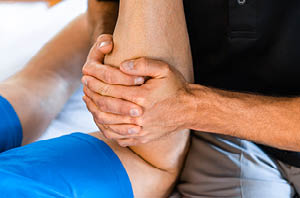 Clinician's hands examining a patient's bent knee during an orthopedic exam
